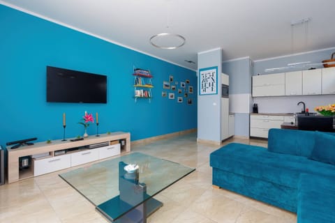 A bright, modern living room with a turquoise sofa, decorative pillows, and a flat-screen TV mounted on the wall.