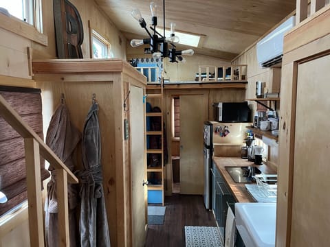Looking down the tiny from the living room, you can see the kitchen, storage closet on the left, bedroom stairs on the left, and a ladder leading to office space.  Bathroom is at the end of the house behind the sliding pocket door 