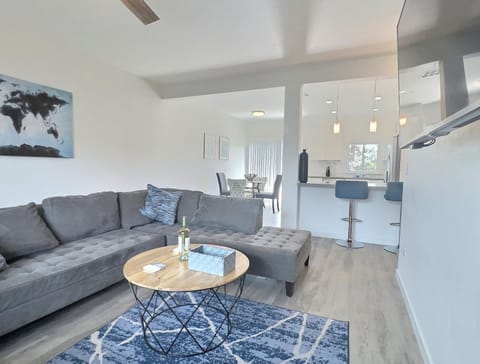 Spacious living room with L-shaped couch, smart TV, open kitchen, dining nook, and patio views (1)