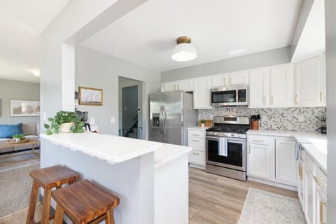 Modern kitchen with stainless steel appliances and gas range   - Bright white cabinets with gold accents and stylish backsplash   - Breakfast bar seating perfect for morning coffee or quick meals