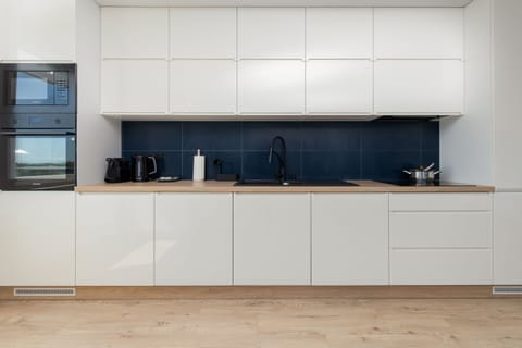 A fully equipped kitchen with sleek white cabinets and a contrasting black backsplash.