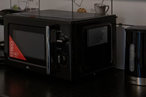 A close-up of a microwave and coffee setup on a sleek black kitchen counter.

