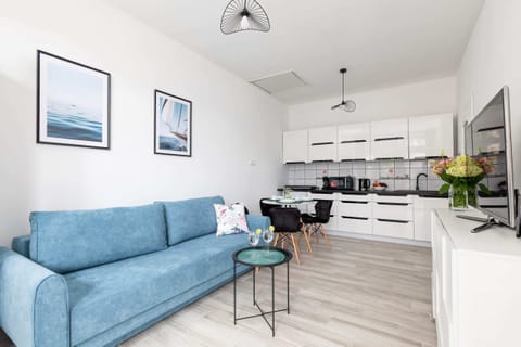 A bright living room with a blue sofa, coffee table, and an open layout connecting to the kitchen.
