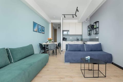 A wide view of the living and dining area with light blue walls, a green sofa, and a modern, open-plan layout.

