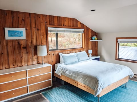 The master bedroom is large and filled with light and warm wood walls.
